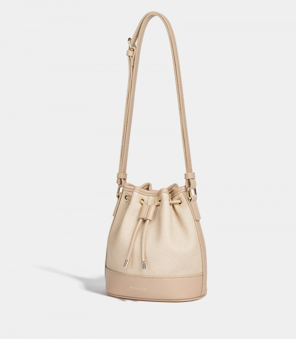 MOSSDOOM Alicia beige bucket bag hanging by its adjustable shoulder strap.