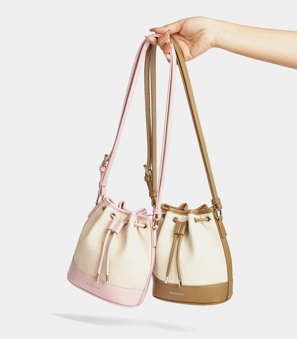 Les deux coloris, rose et marron, du sac seau MOSSDOOM Alicia tenus à la main.